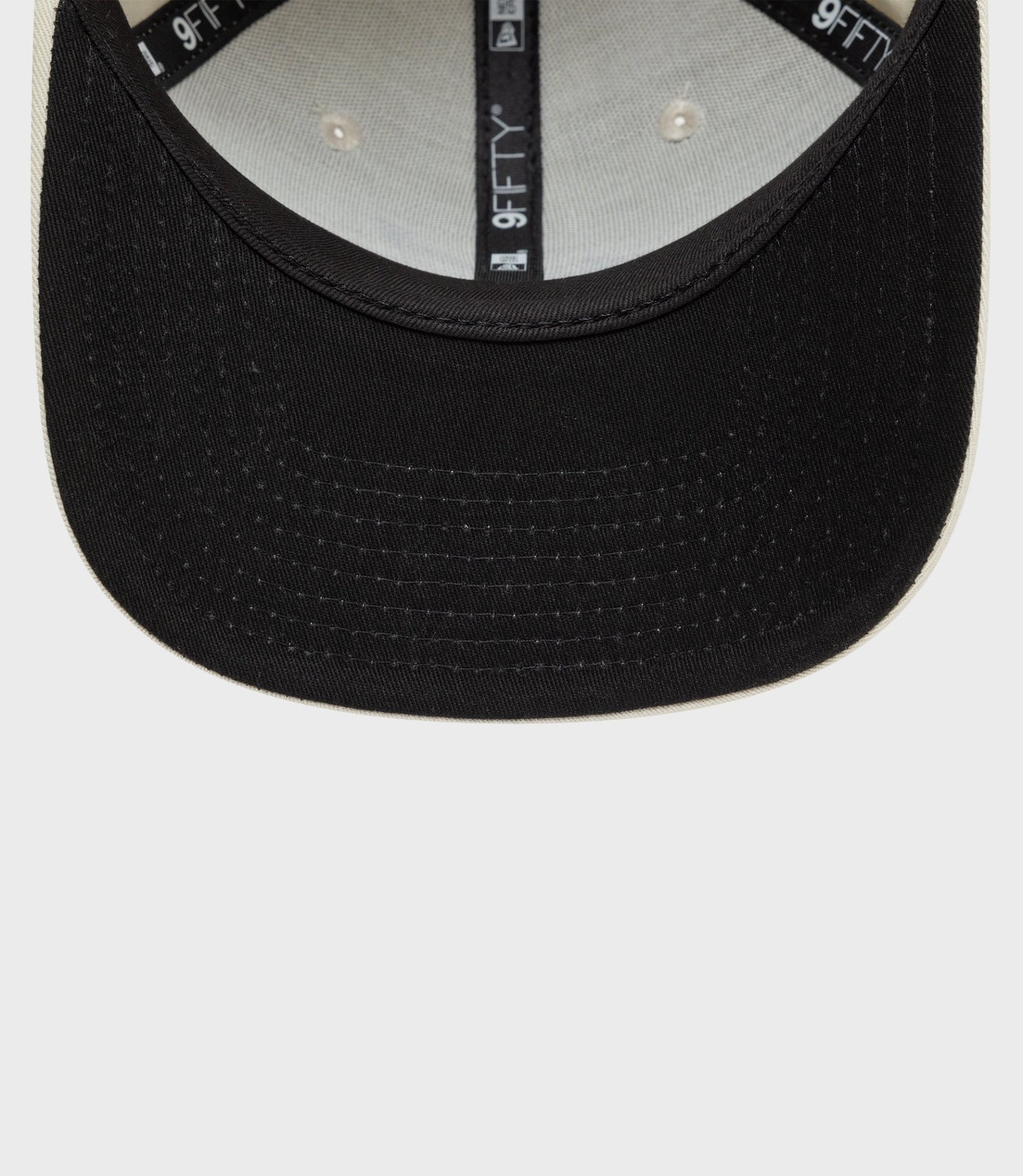 Close up of New Era Alpine 9Fifty pre curved cap in black with tan edge showing brim stitching and interior 9FIFTY branding
