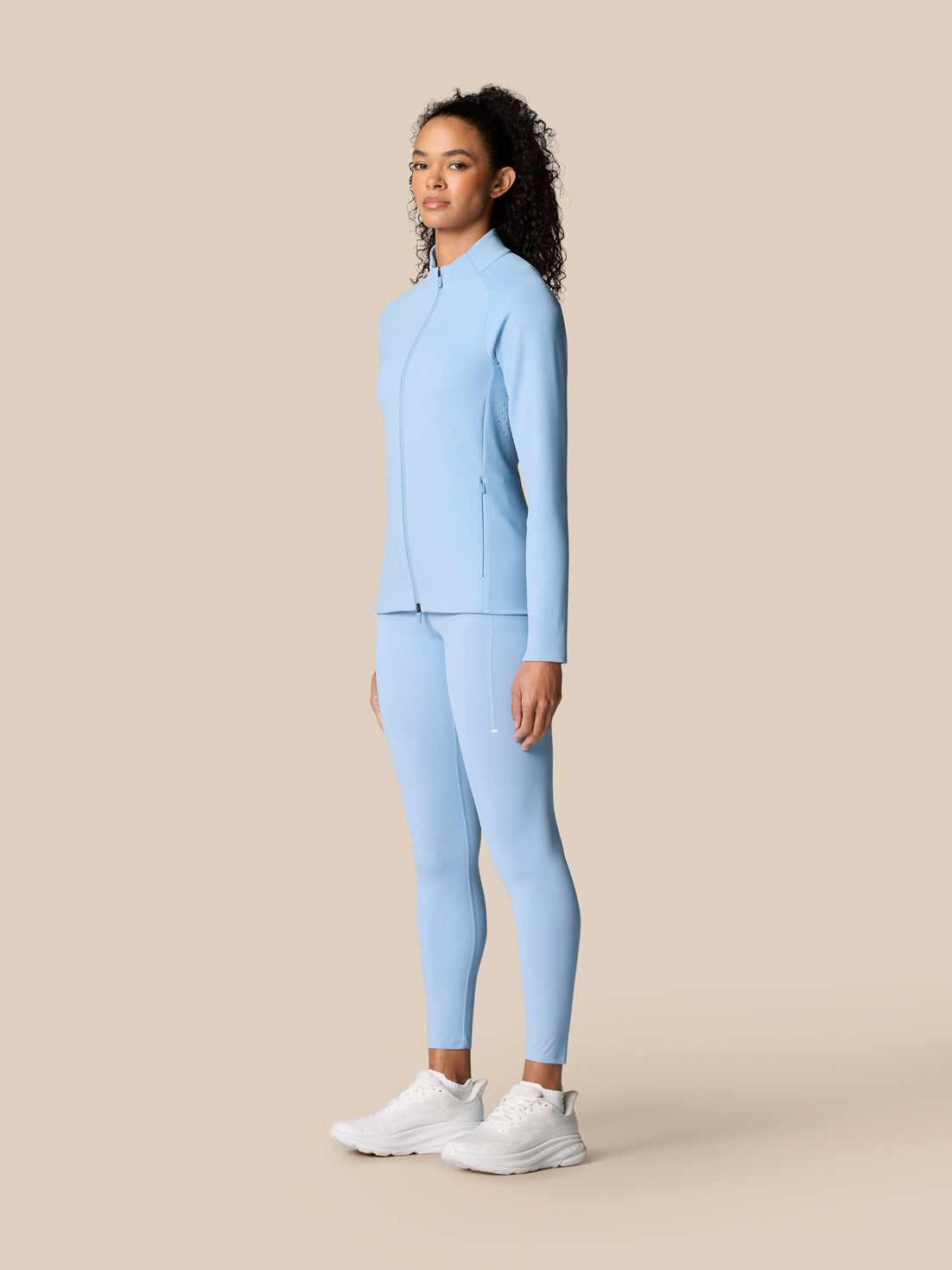 Full-body side view of a woman in sky blue Zone Training jacket and matching leggings.