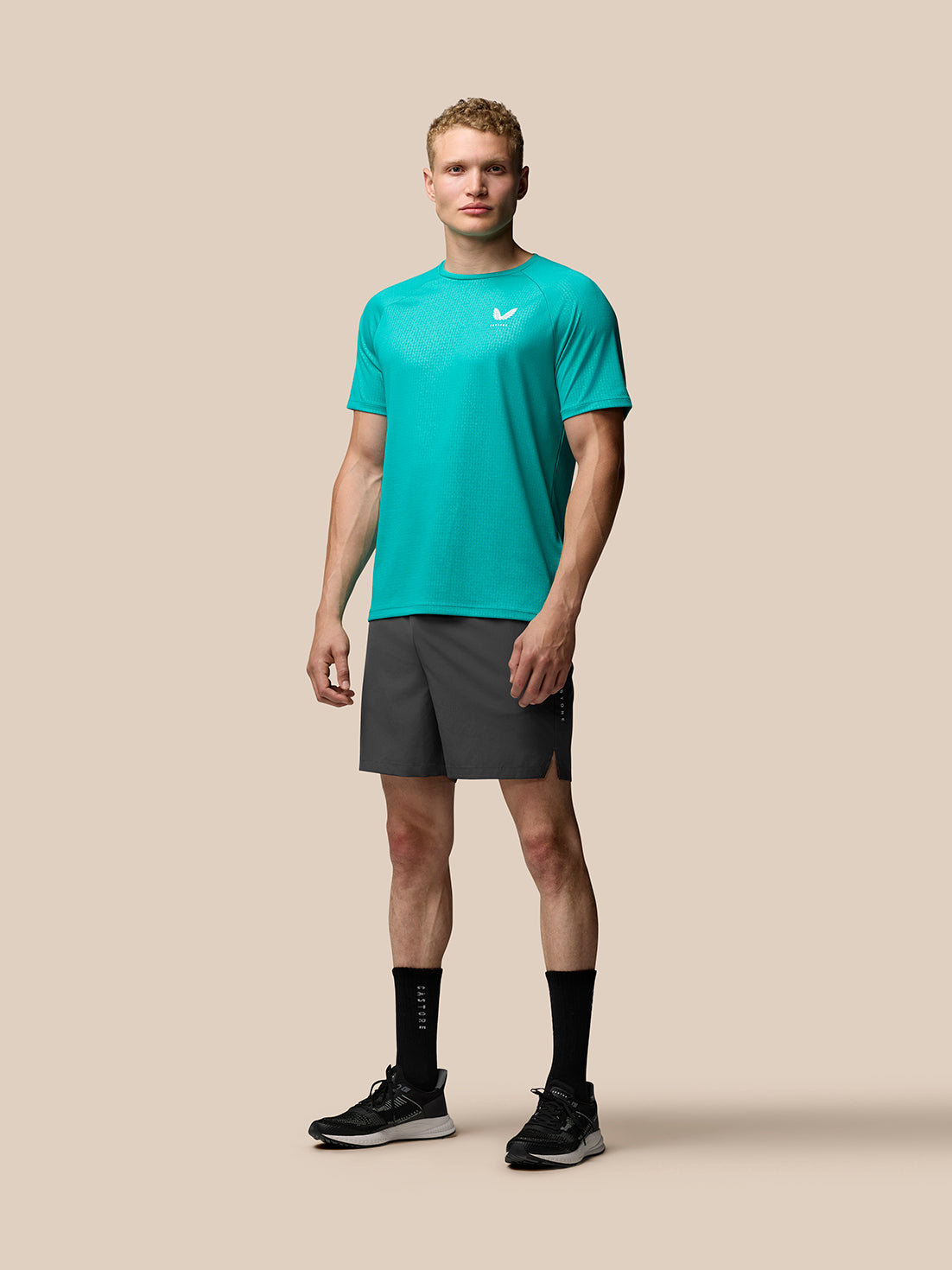 Full-length portrait of a man in teal training tee and black shorts with Castore logo on the thigh.