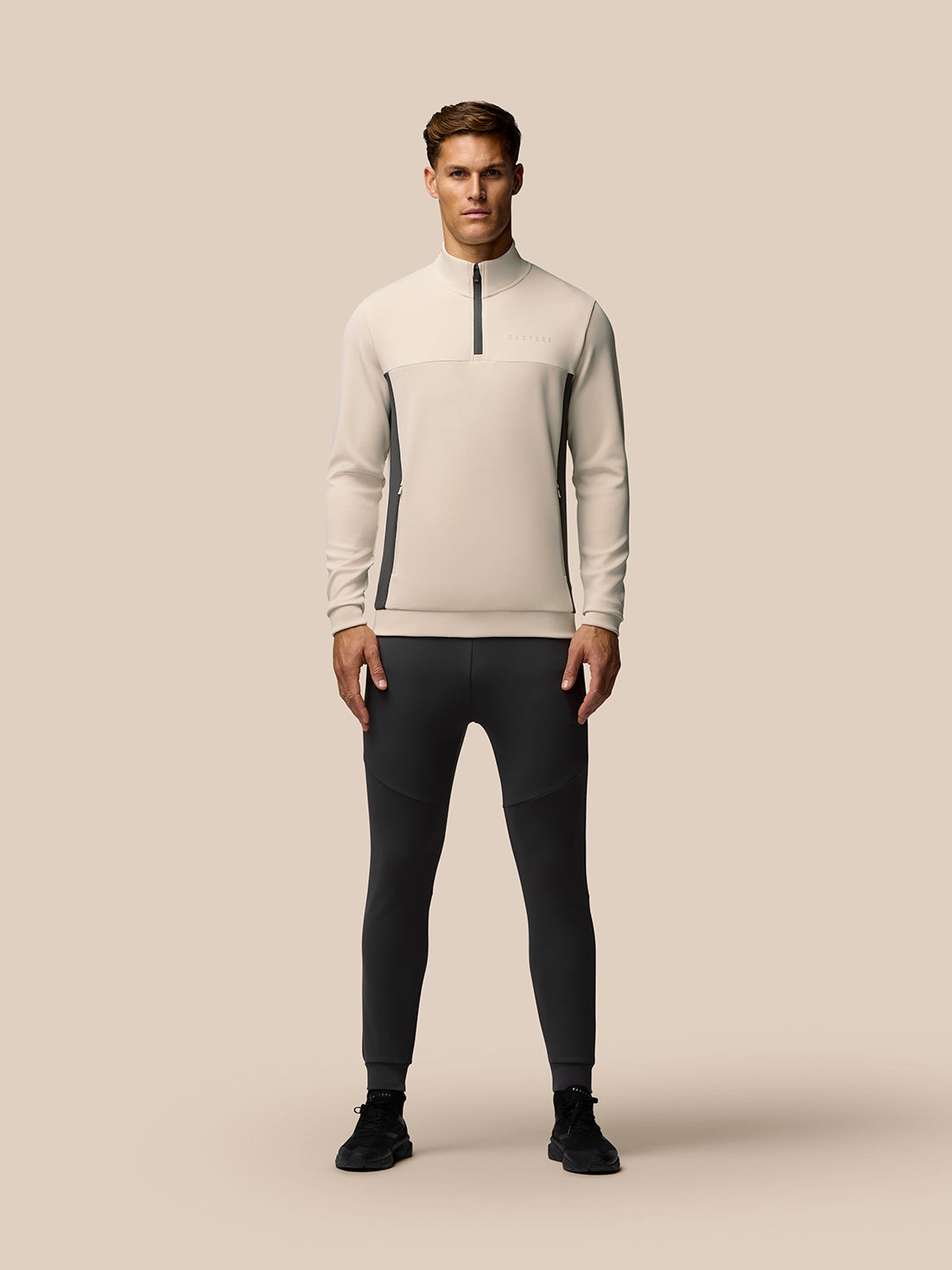 Male model wearing Beige Flex Lifestyle 1/4 Zip top with stand collar and zip pockets, paired with dark athletic pants