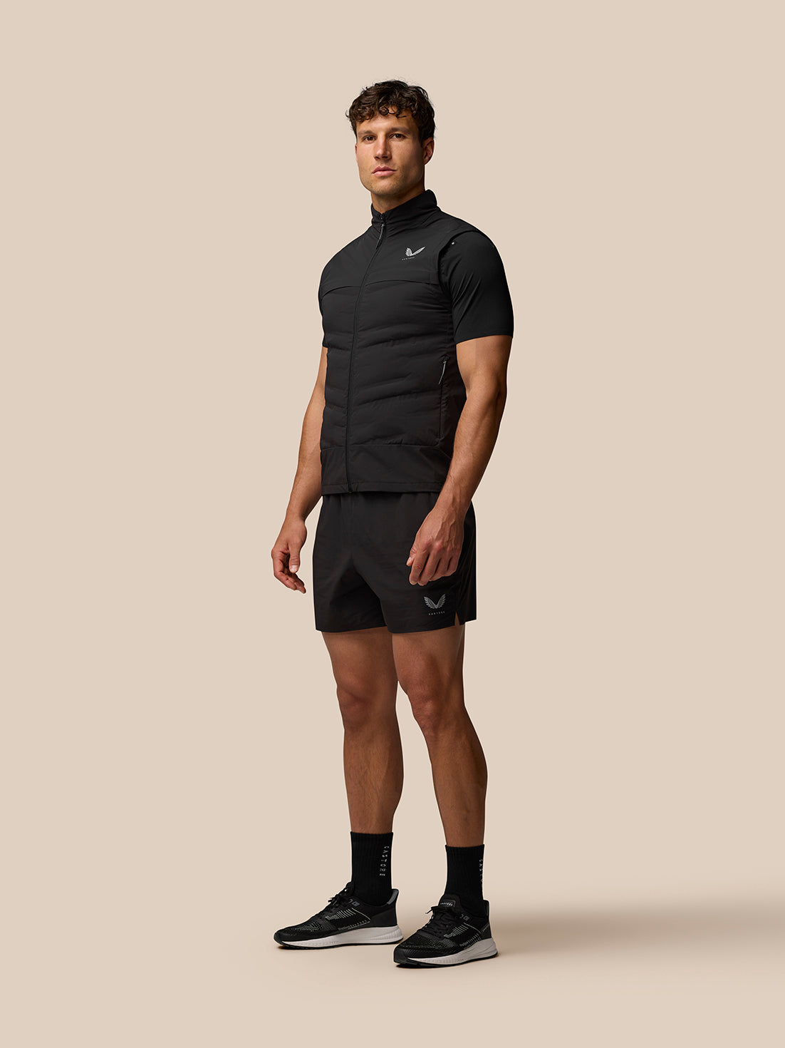 Full-body view of a male model wearing the black Zone Training Gilet over a black tee with matching shorts and sneakers