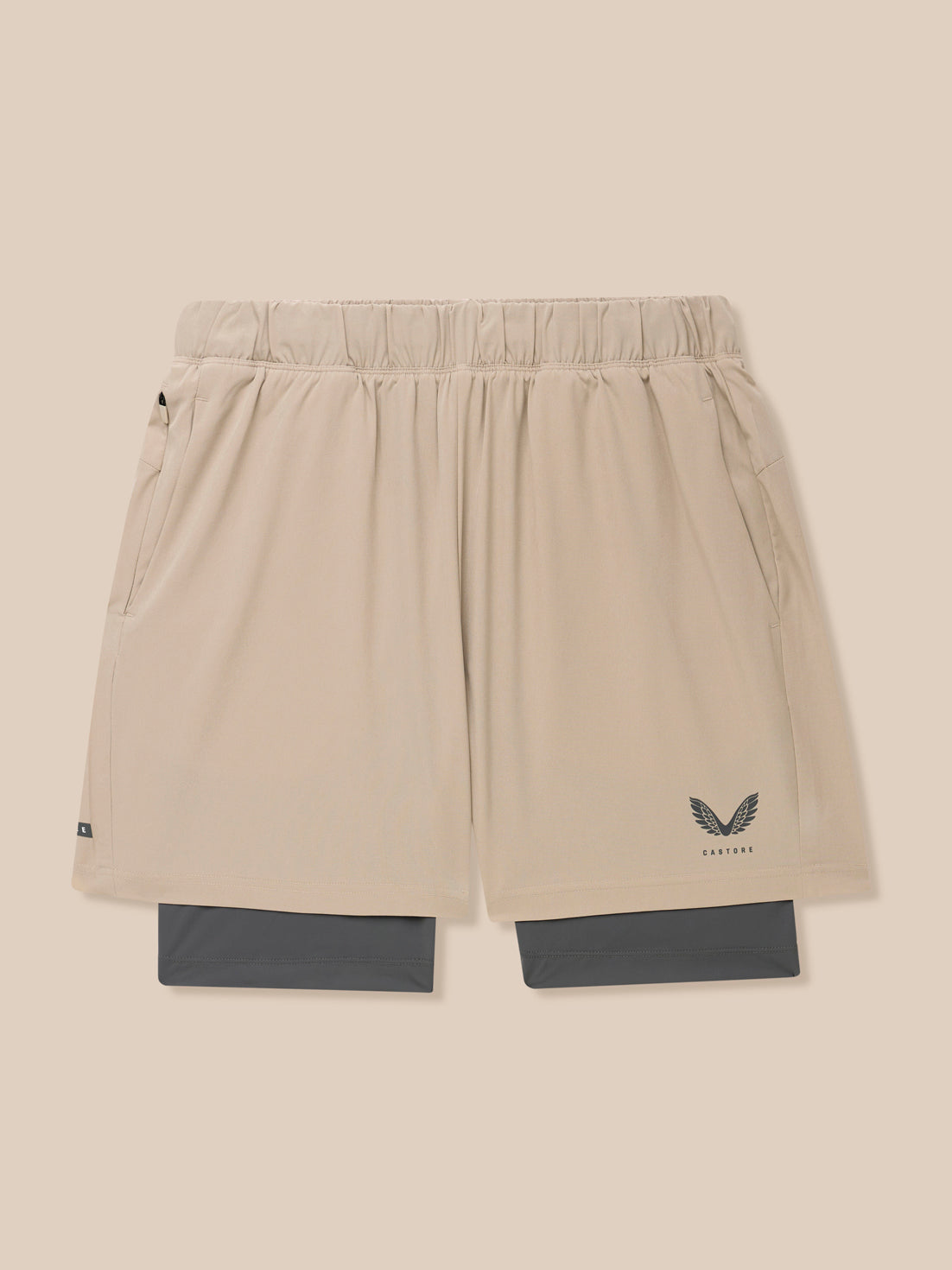 Beige Flow 2-in-1 shorts with blue undershorts peeking from the hem and Castore logo on the leg