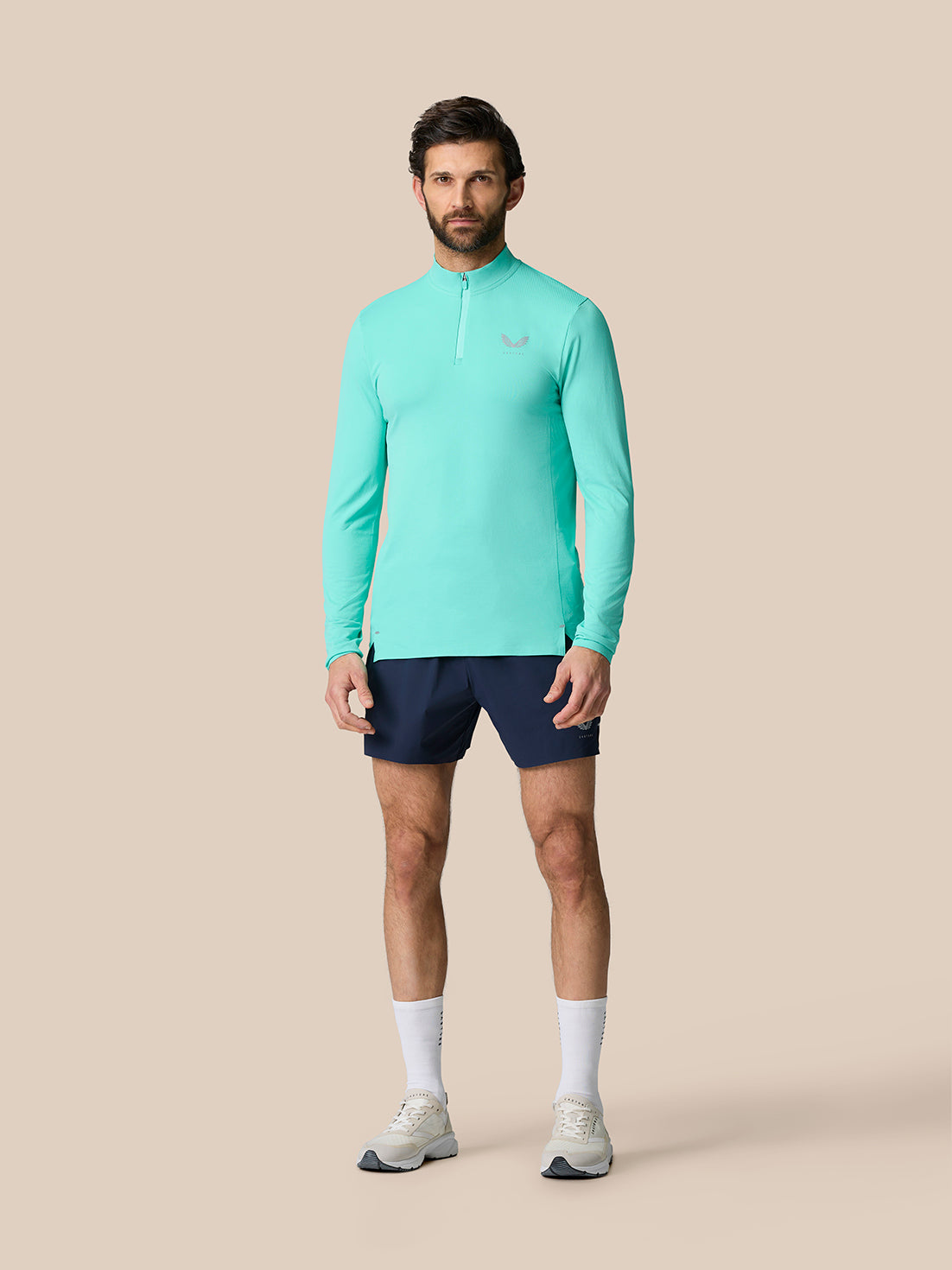 Full-length view of a man wearing teal Zone Training 1/4 zip top with white wing logo on the chest and navy shorts
