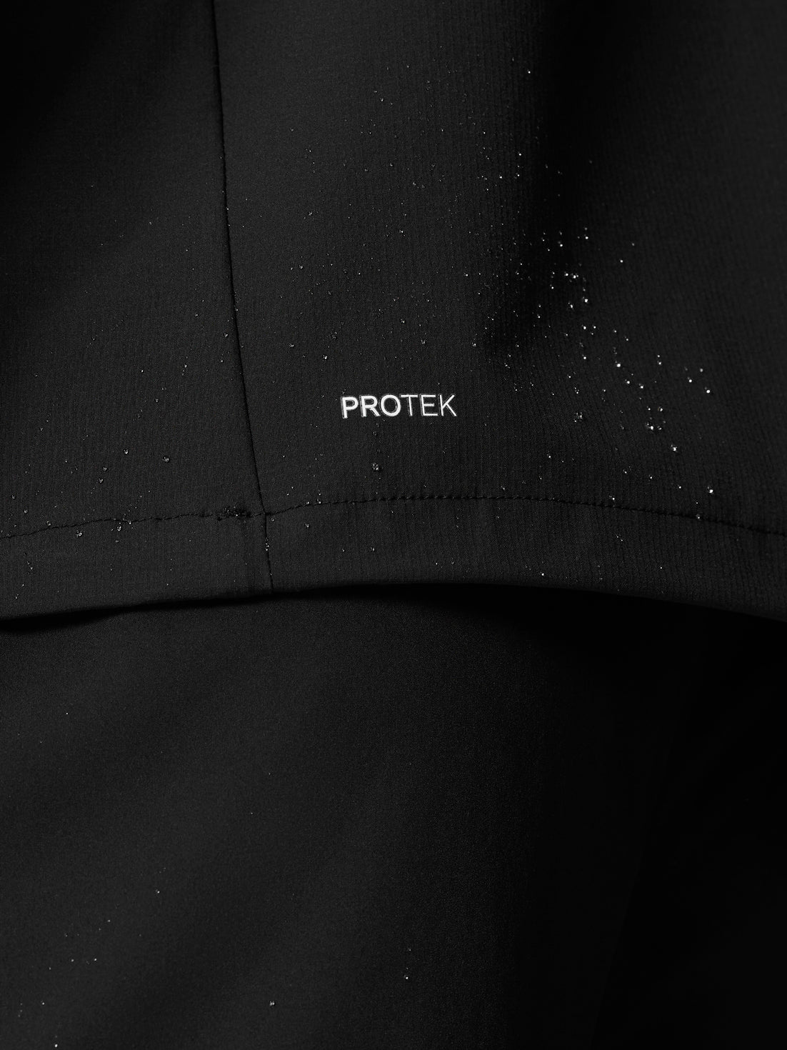 Close-up of black Flow Training Hoodie fabric with ProTek branding and water droplets.