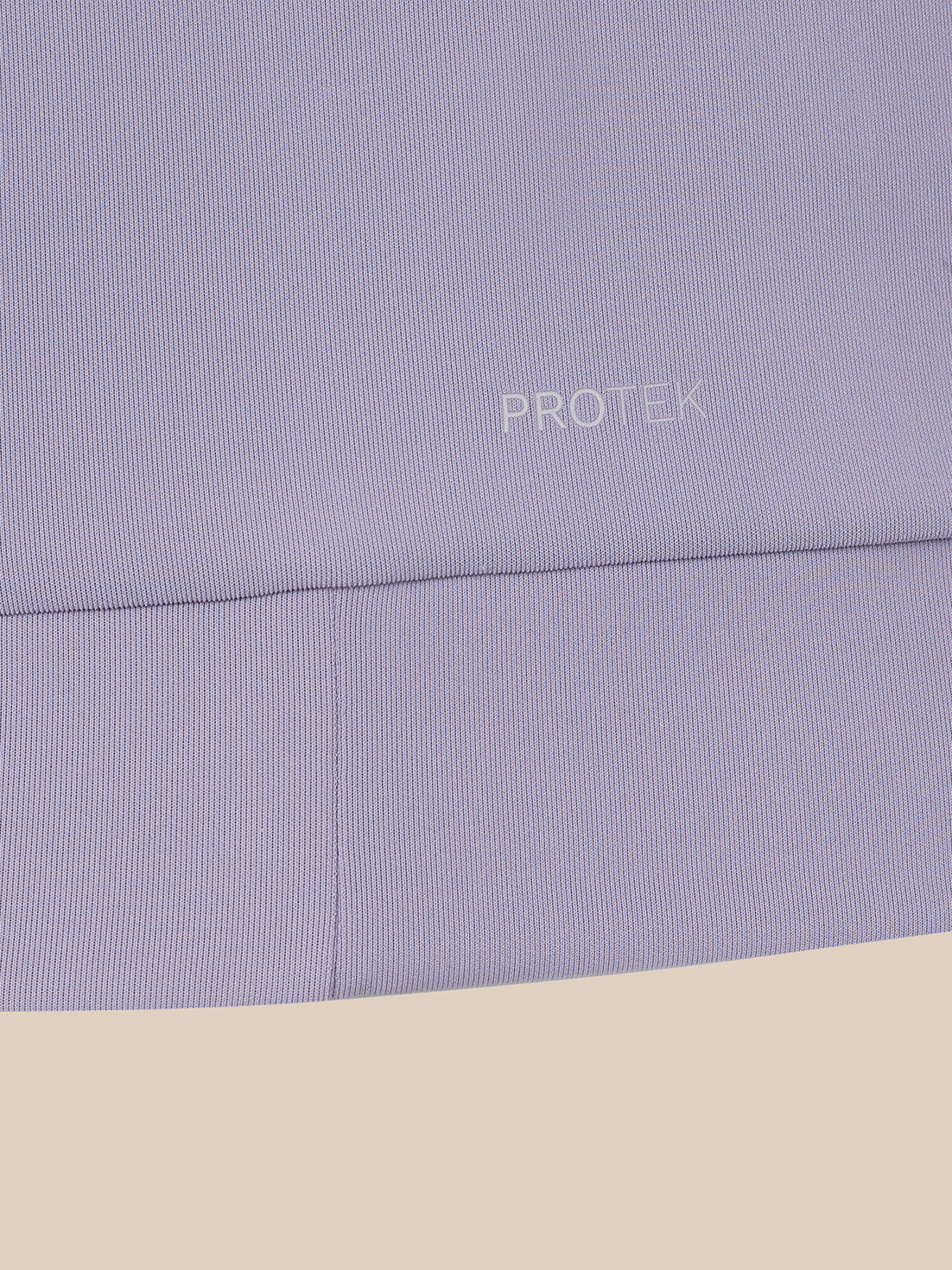 Close-up of a light lavender ribbed fabric with the word PROTEK printed in small white text, shown against a beige background.