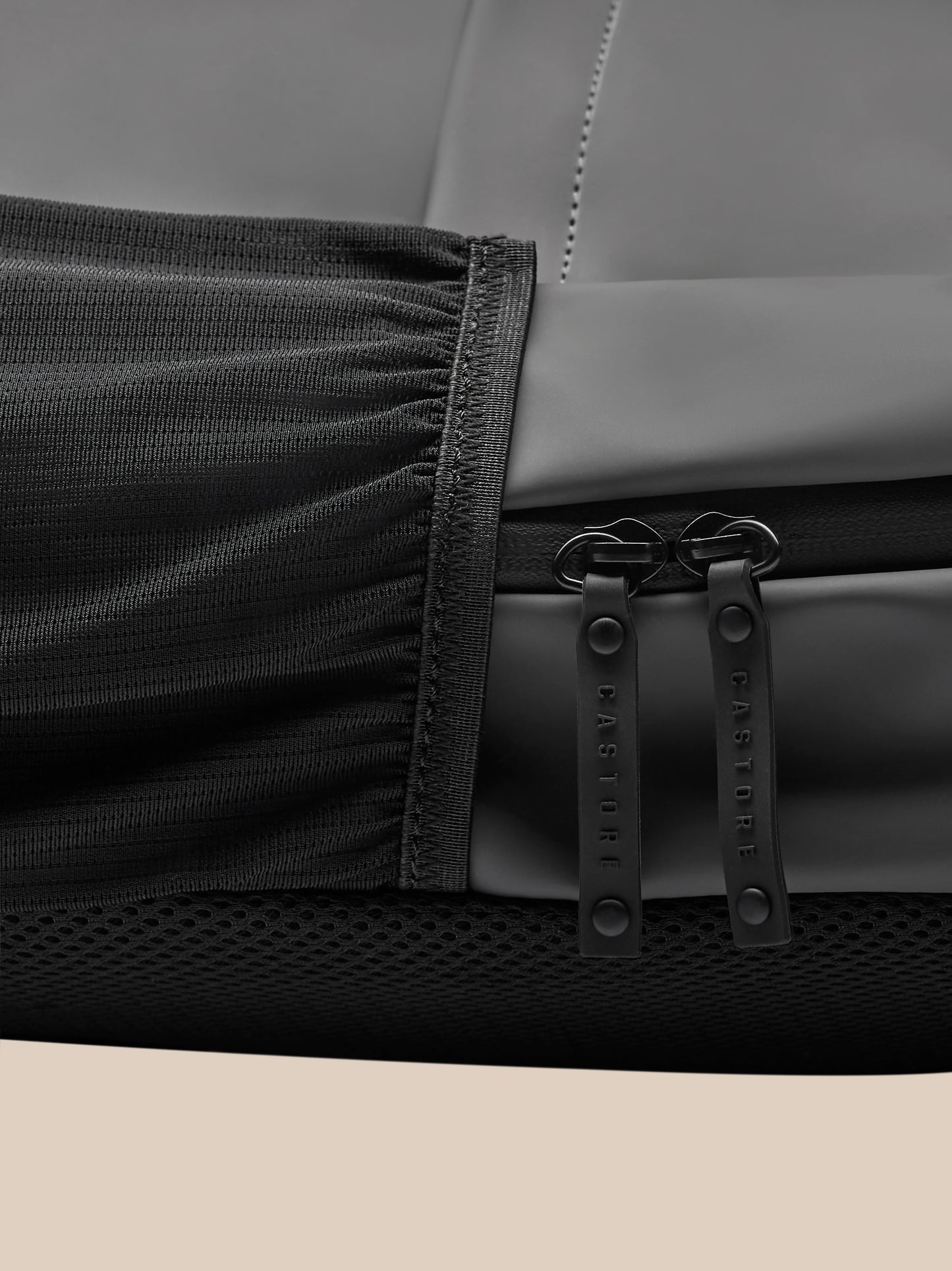 Close-up of gunmetal Core Backpack fabric with dual zipper pulls branded Castore and rugged edge stitching