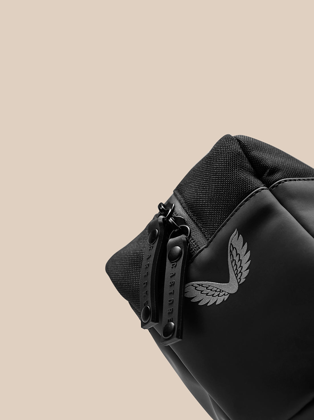 Close-up of black Active Wash Bag showing rugged zipper, textured fabric, and wing logo against a tan background.