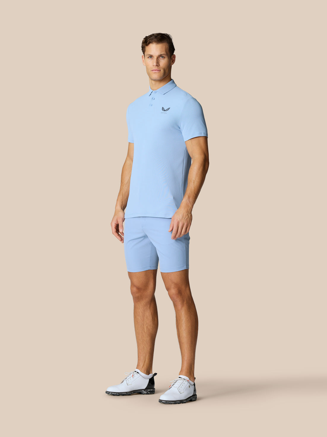 Male model in sky blue Golf Club Essential Polo with matching shorts and Castore emblem on chest