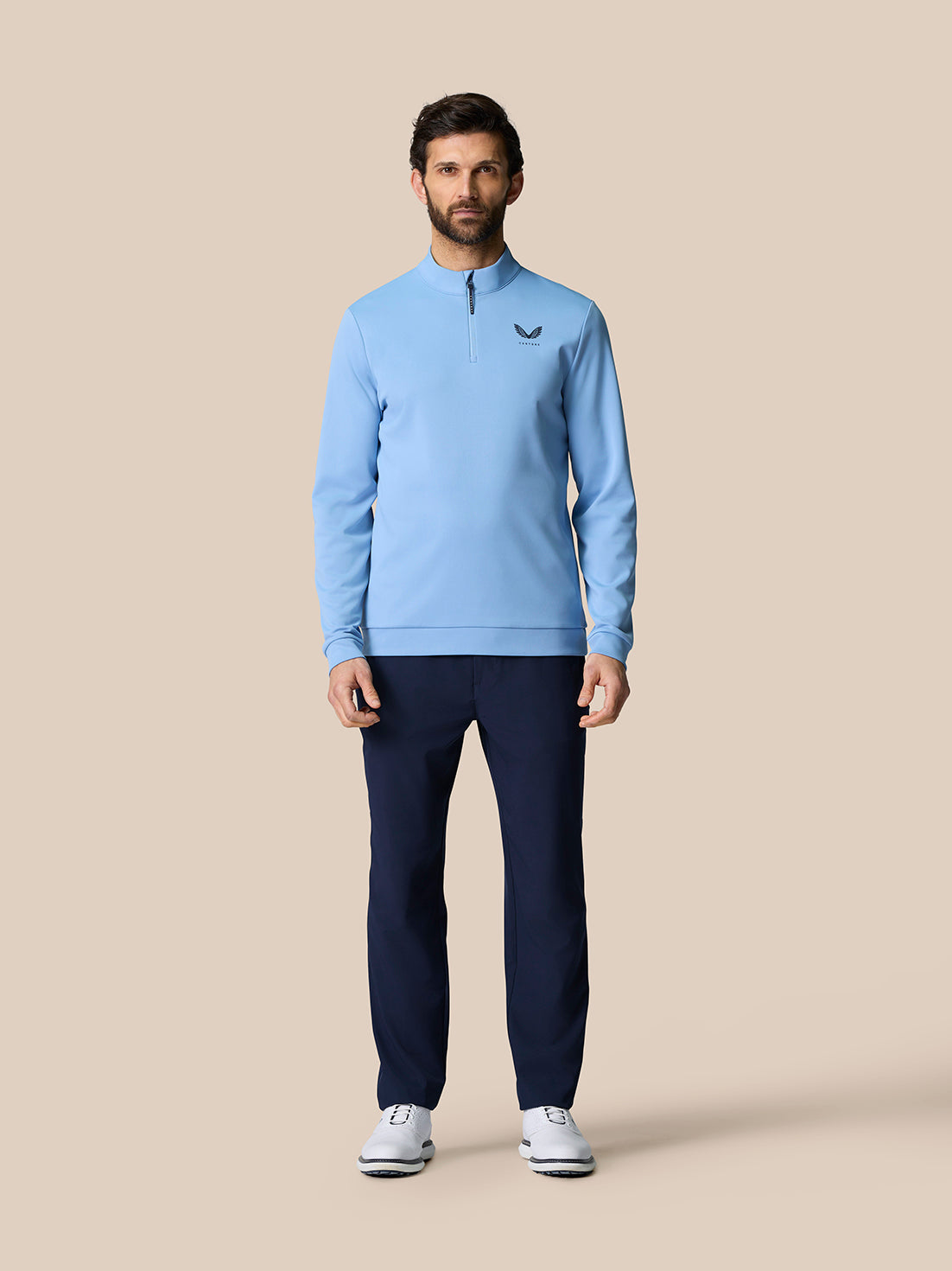 Male model wearing sky blue Golf Club Classic quarter zip top with stand collar on beige studio backdrop