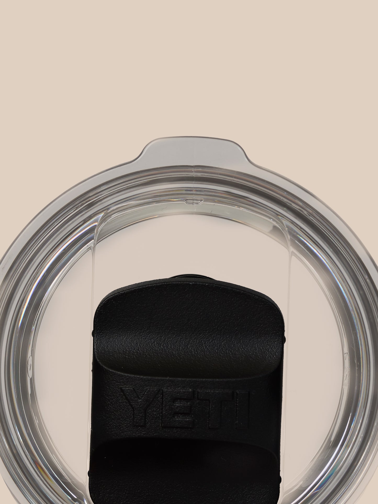 Close-up of the lid area on a YETI x Castore 300ml tumbler with a curved clear lid against a beige background