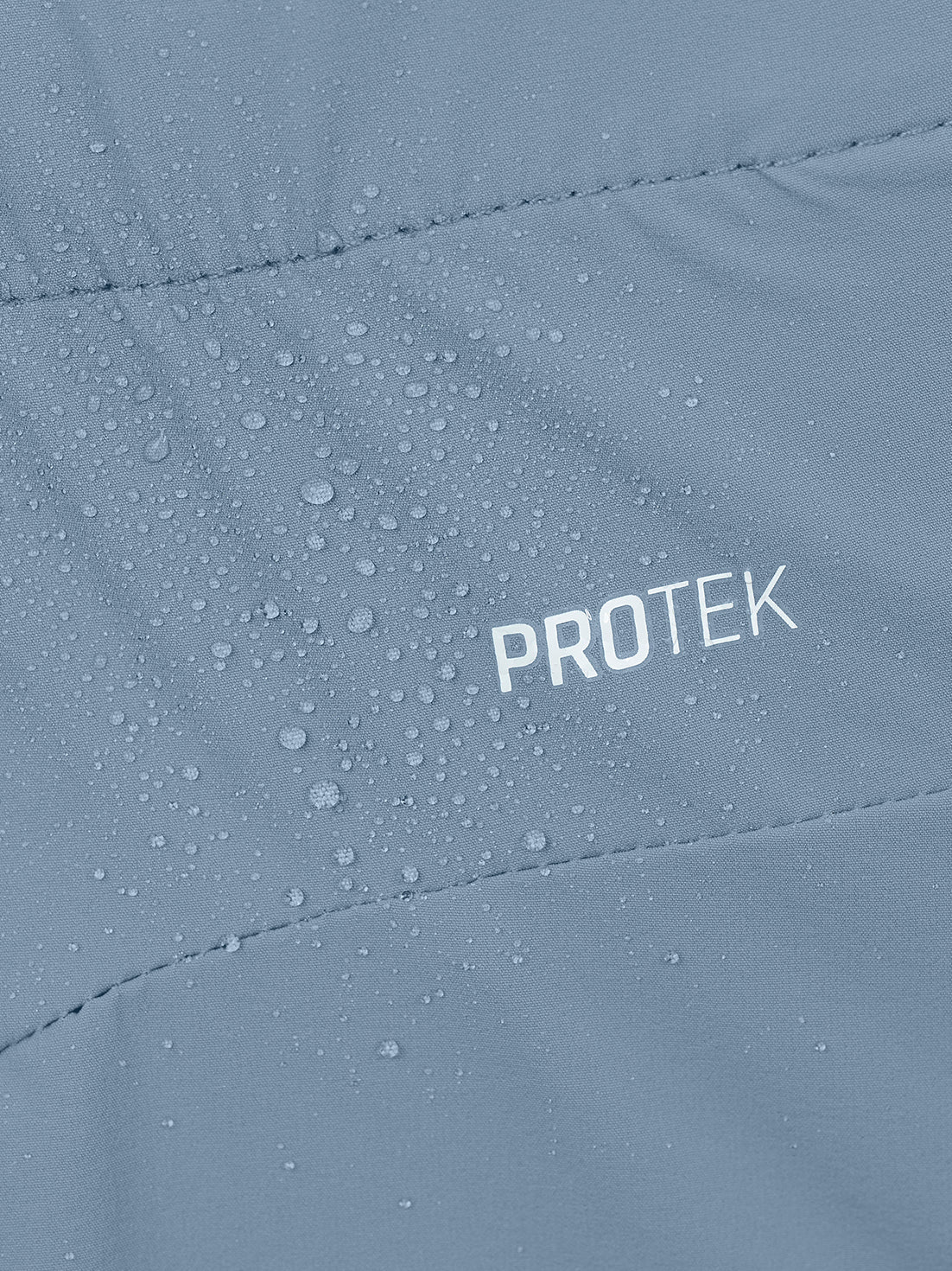 Close-up of a light blue-gray waterproof jacket with water droplets on the surface and the word PROTEK printed in white.