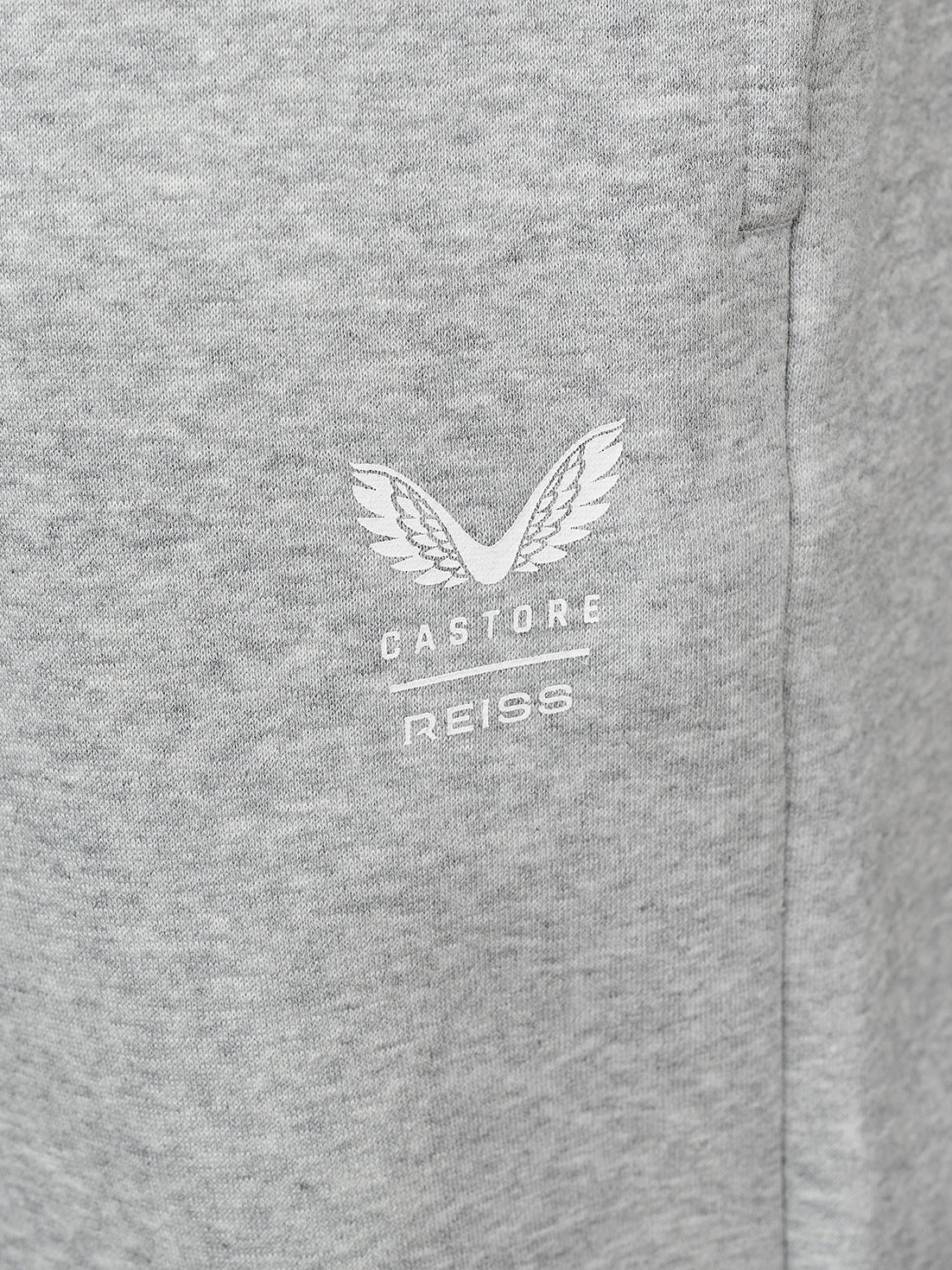 Close-up of a heather gray fabric surface with a small white embroidered winged logo and the text 'CASTORE REISS' centered on the chest.