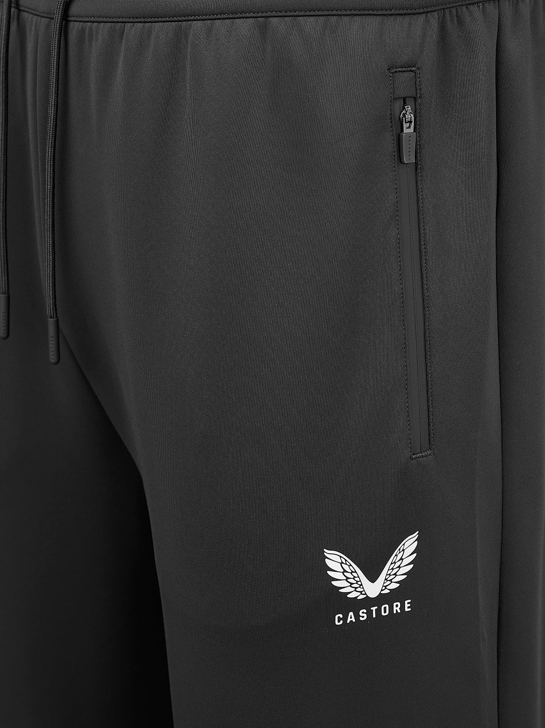 Close-up of black athletic pants showing a side zip pocket and a white Castore wing logo on the lower leg.
