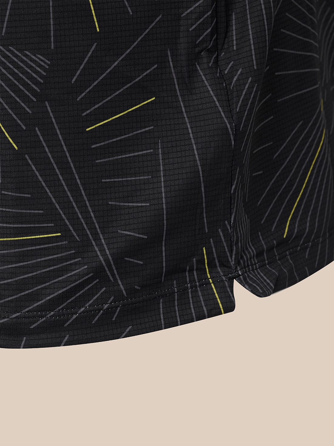 Close-up of black athletic shorts with a geometric line pattern in gray and bright yellow, shown against a solid beige background.