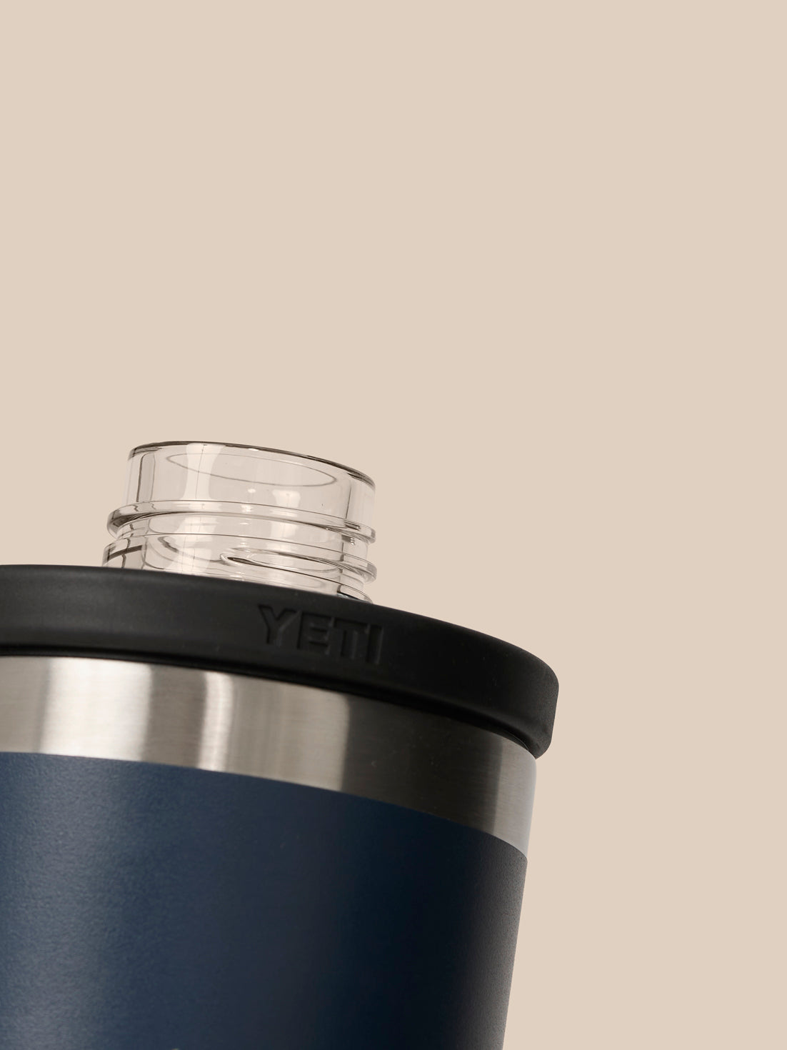 Close-up of YETI water bottle neck with clear cap and navy body against a beige background