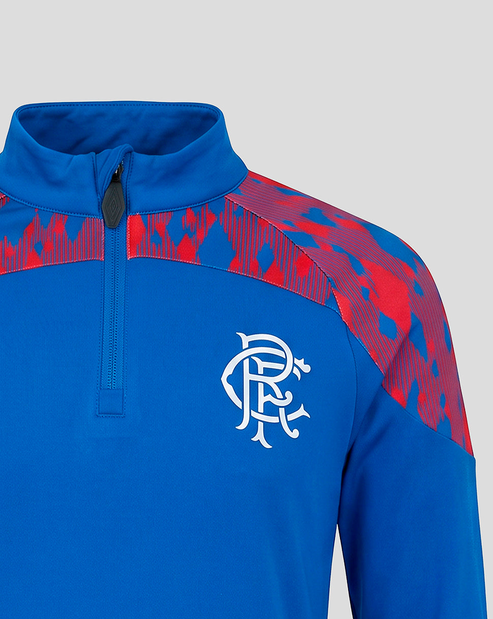 A close-up of a royal blue quarter-zip athletic pullover with red patterned shoulder panels and a white Rangers FC crest on the chest, shown against a light gray background.