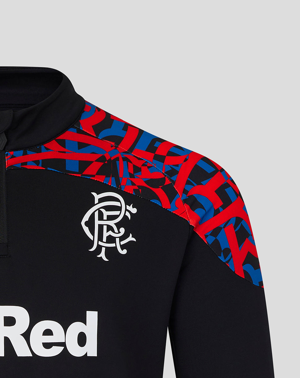 Close-up of a black long-sleeve sports top with a red and blue geometric pattern across the shoulders and upper chest, a white Rangers FC crest on the chest, and part of a white 'Red' sponsor logo on the front, set against a light gray background.