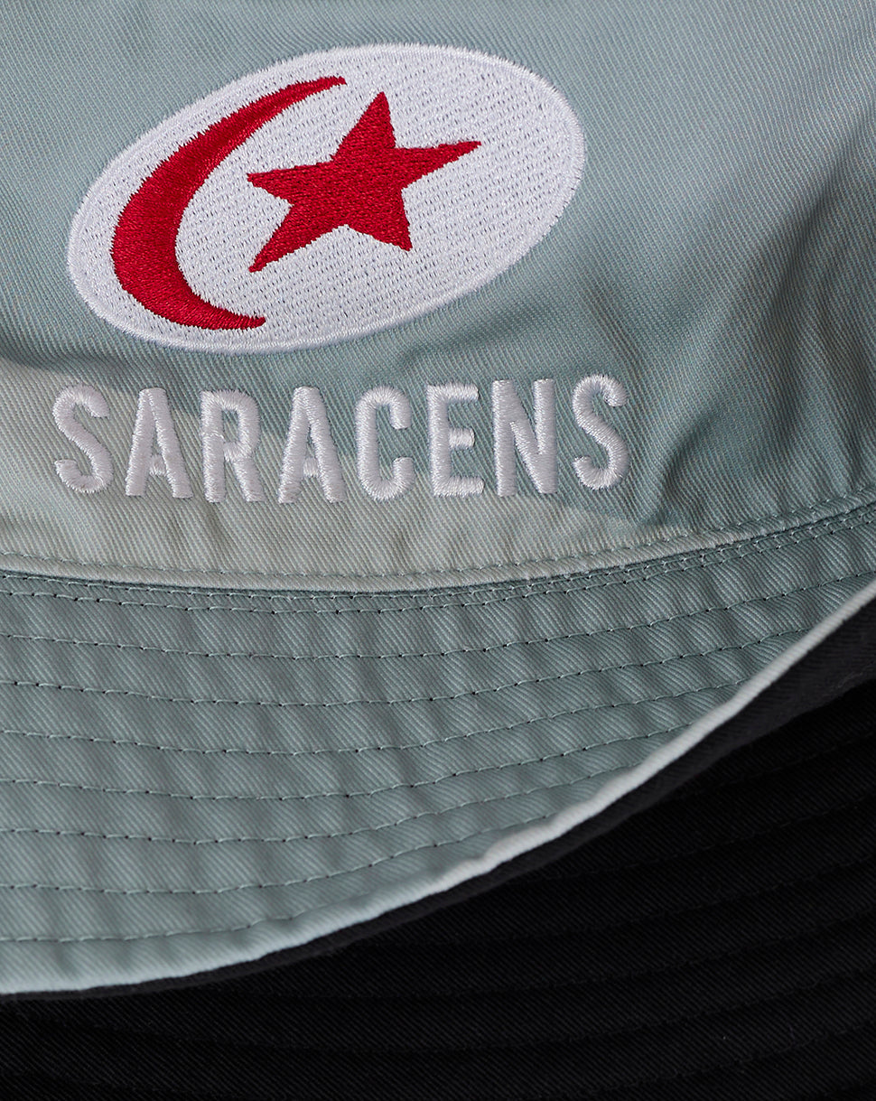 Close-up of teal fabric with a white circular patch showing a red crescent and star and Saracens embroidery.