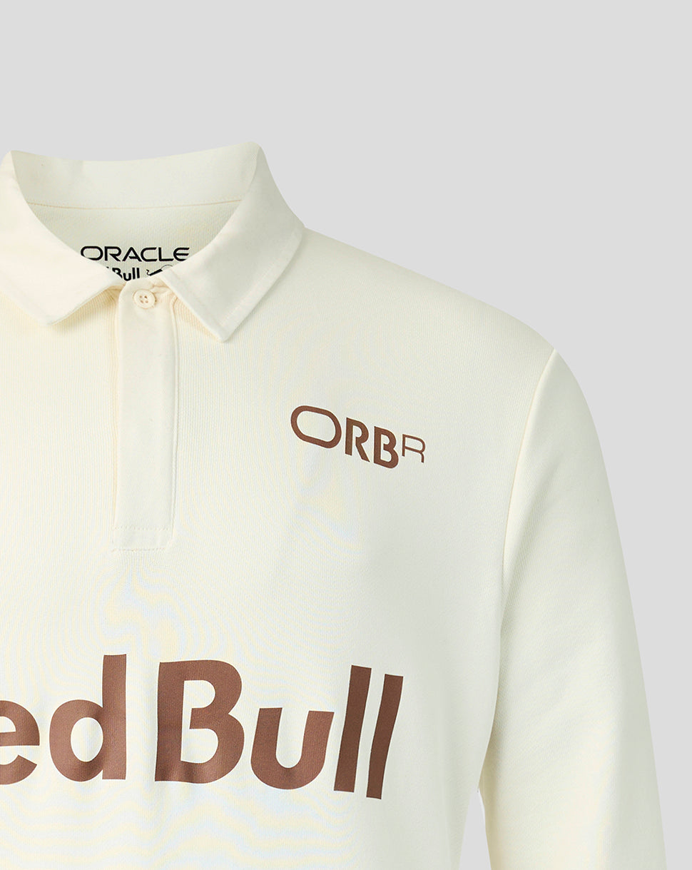 Close-up of a cream-colored long-sleeve polo shirt featuring a brown 'ORBR' logo on the chest and a large 'Red Bull' sponsor logo across the lower front, with 'ORACLE' visible inside the collar.