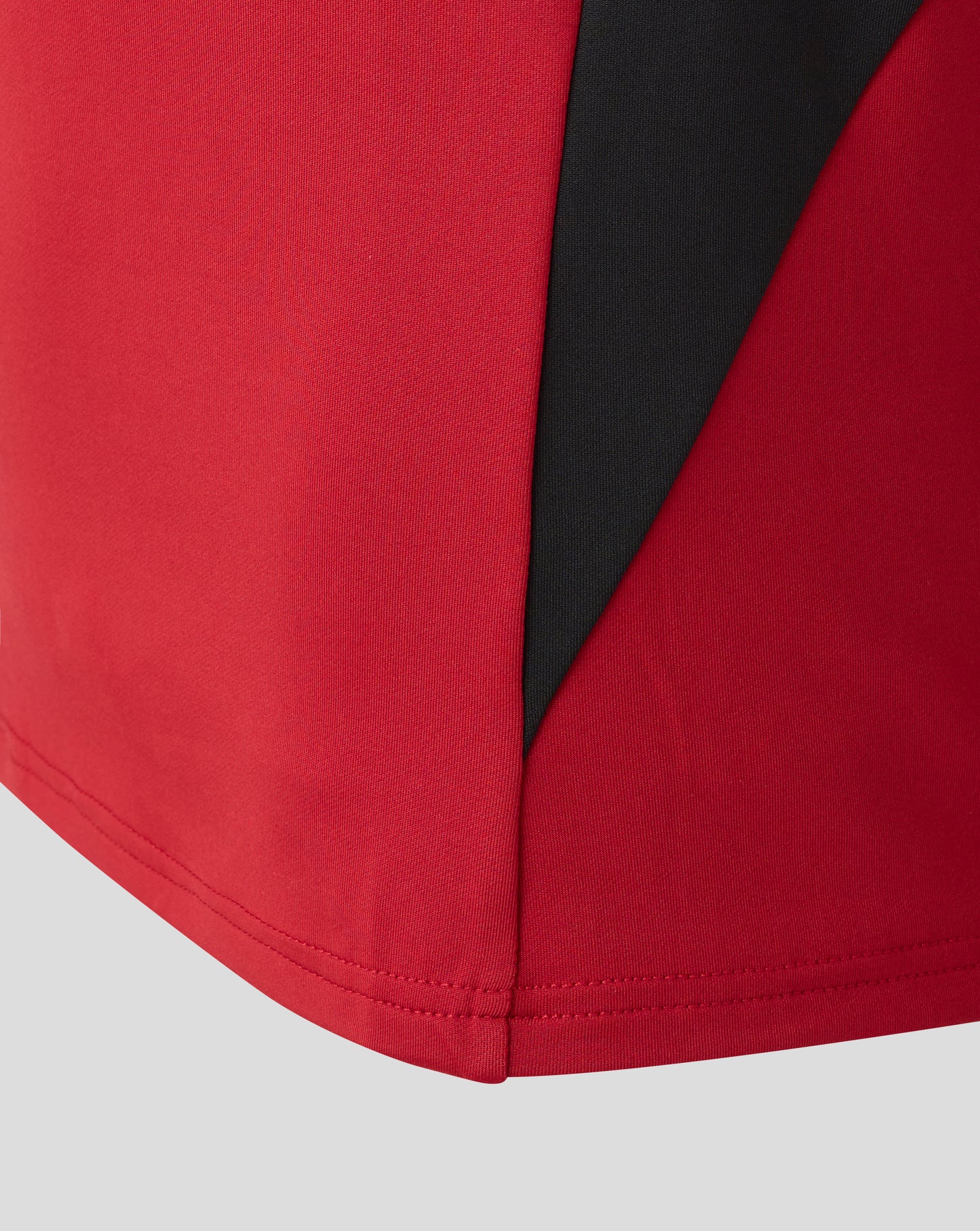 Front close-up of red Saracens training drill top showing a bold black diagonal side panel.