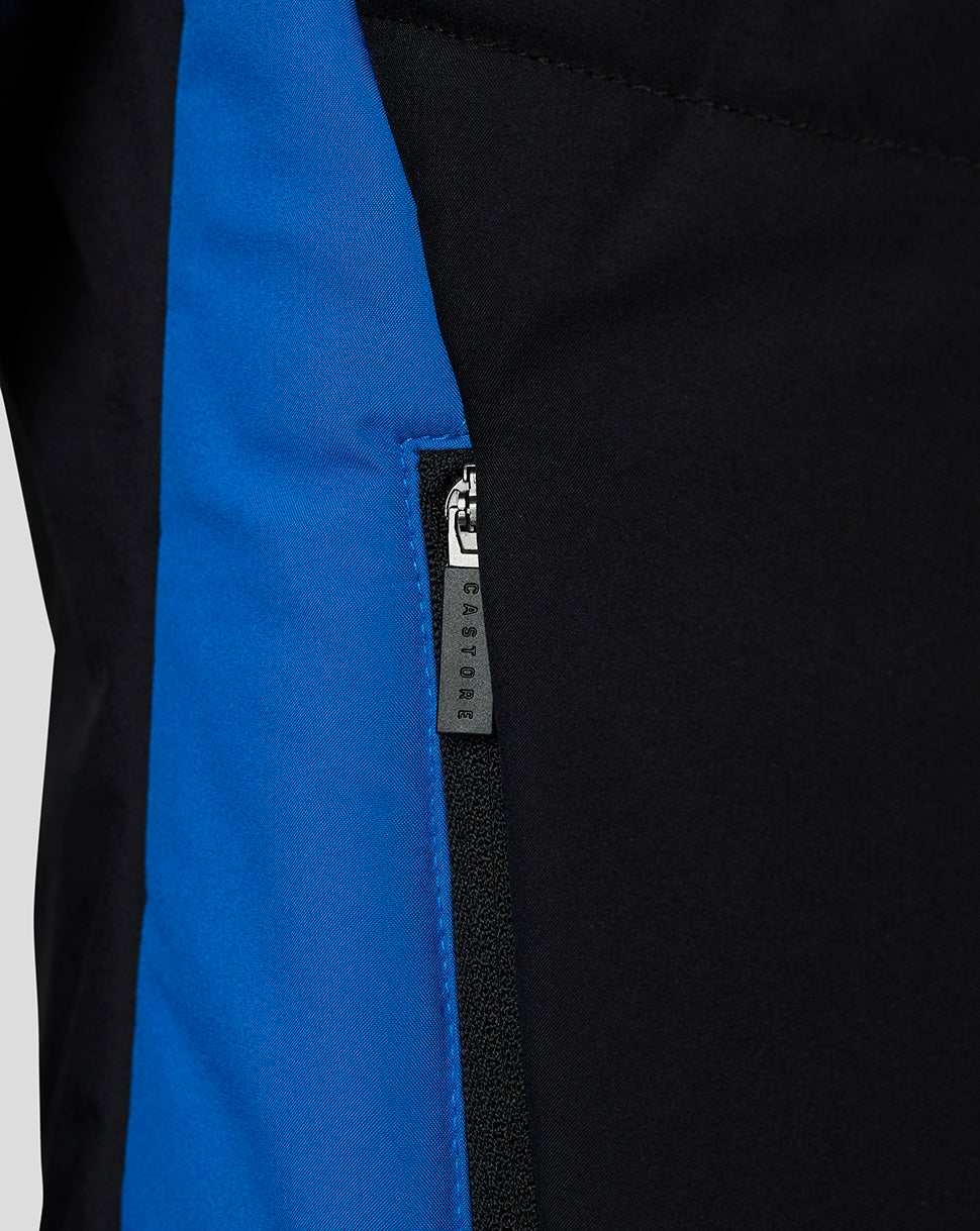Chest view of black jacket showing a white club crest and a blue side panel along the seam.