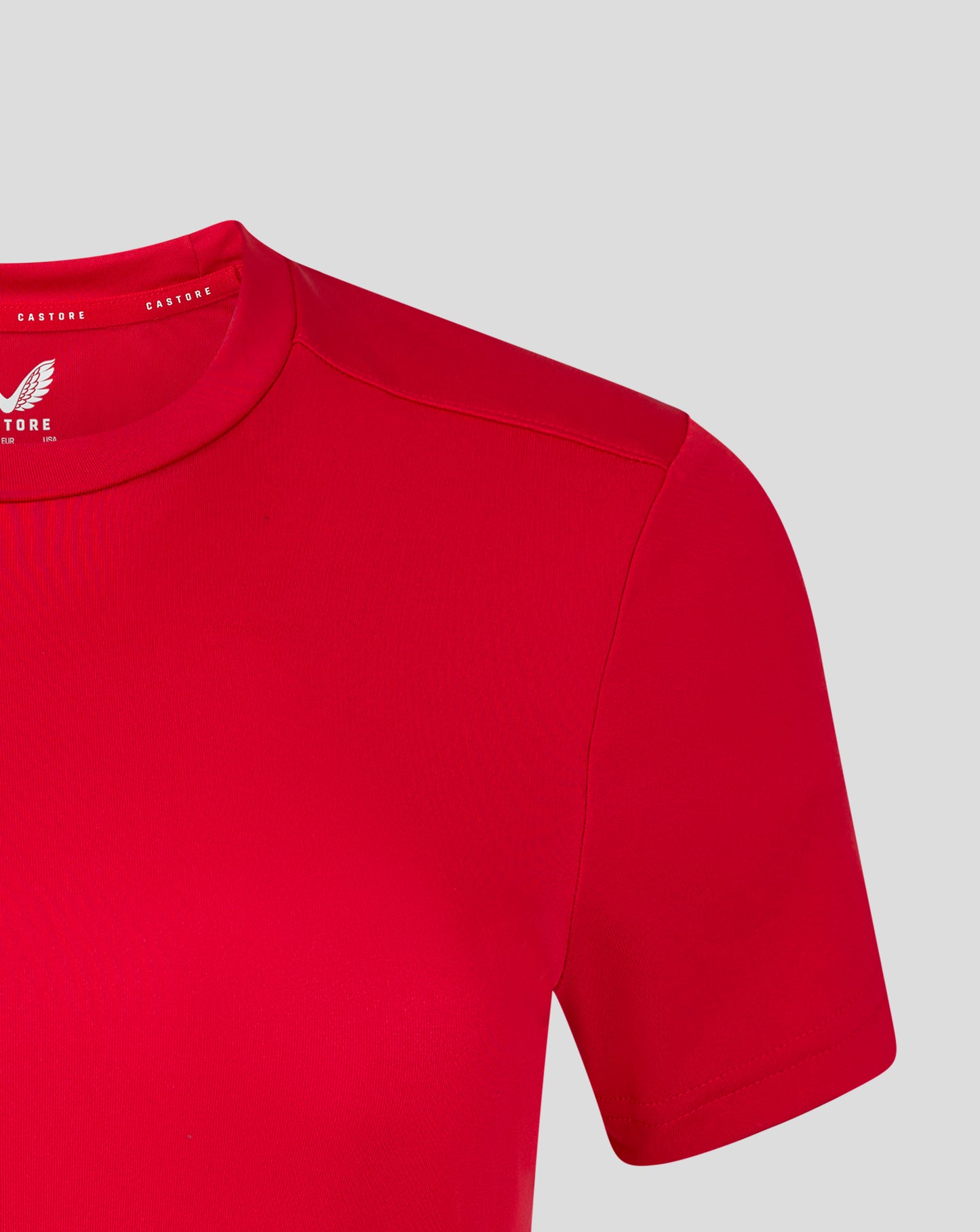 Shoulder and sleeve area of the red performance tee with visible stitching and wing logo on the chest