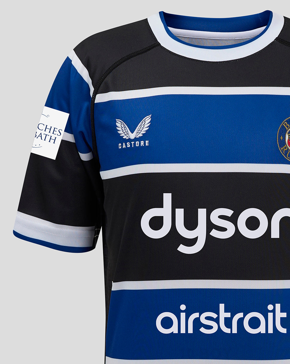 Chest area of Bath Rugby Junior Home Shirt with blue stripe, team crest and sponsor logos.