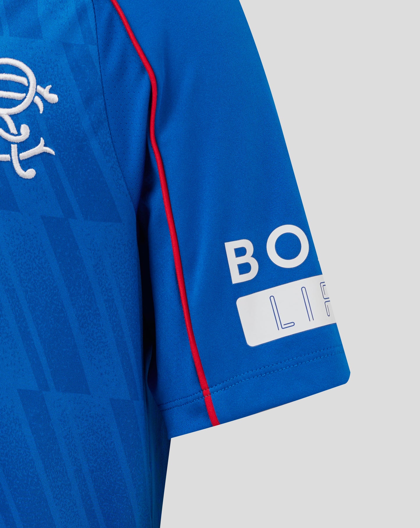Close-up of blue Rangers junior home shirt with crest on chest and Castore branding, plus red piping along the sleeve seam.