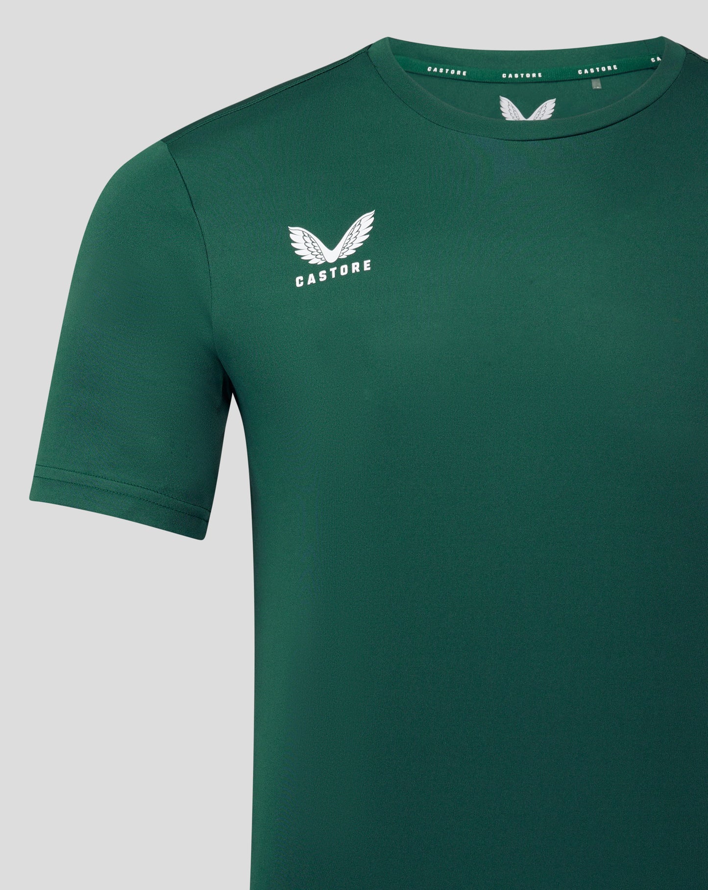 Close-up of forest green tee front showing the white Castore wing logo on the left chest and collar detailing.