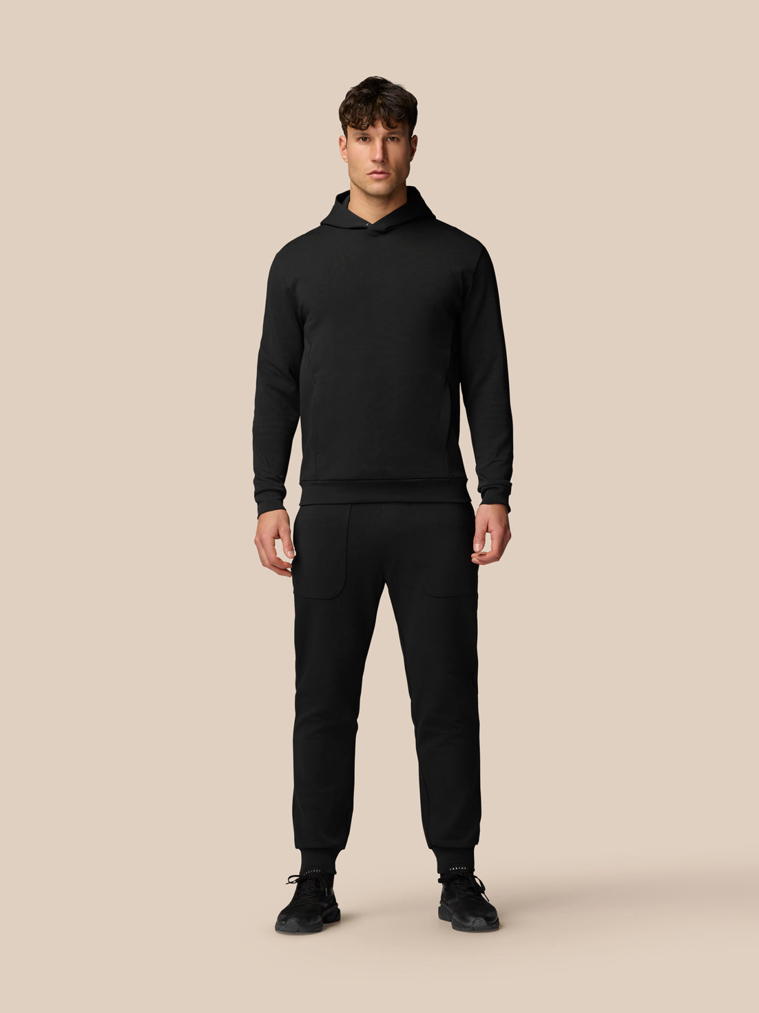 Male model in black Travel Logo Hoodie with three piece hood and center chest branding