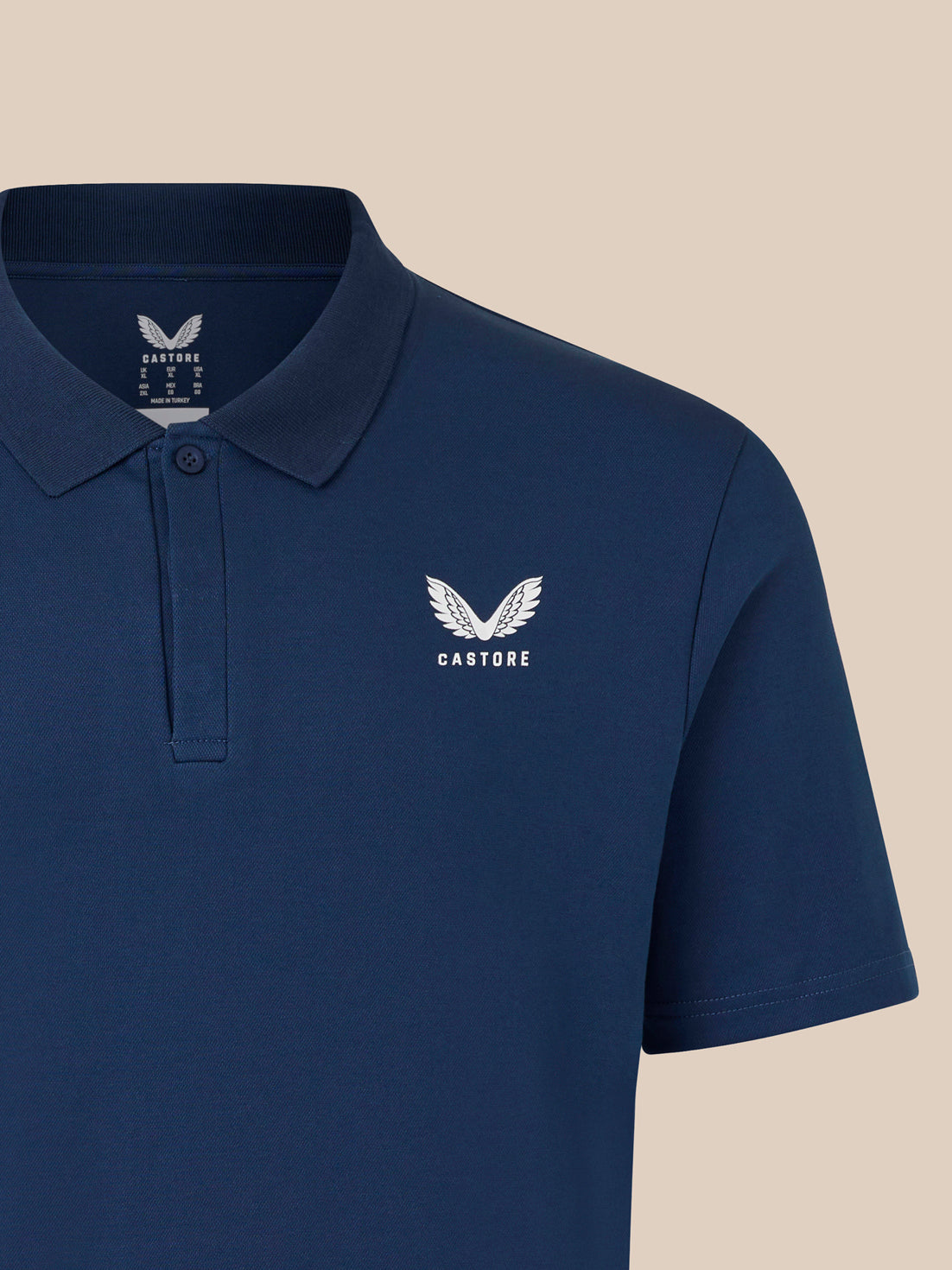 Close up of navy polo shirt with a white crest logo on the left chest.