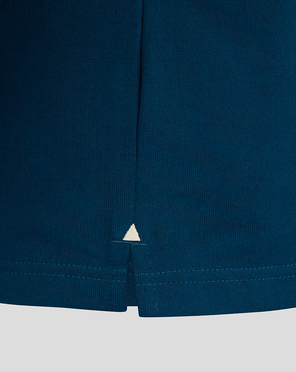 Lower hem of teal Bath Rugby jersey showing side seam split and small white triangle embroidery.