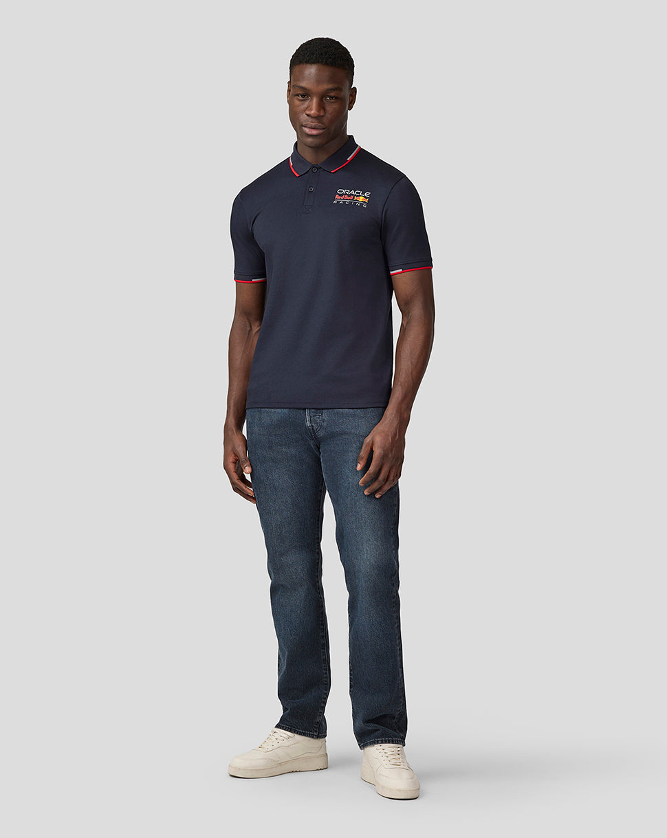 Full body shot of model in navy polo with chest logo, paired with jeans and beige sneakers