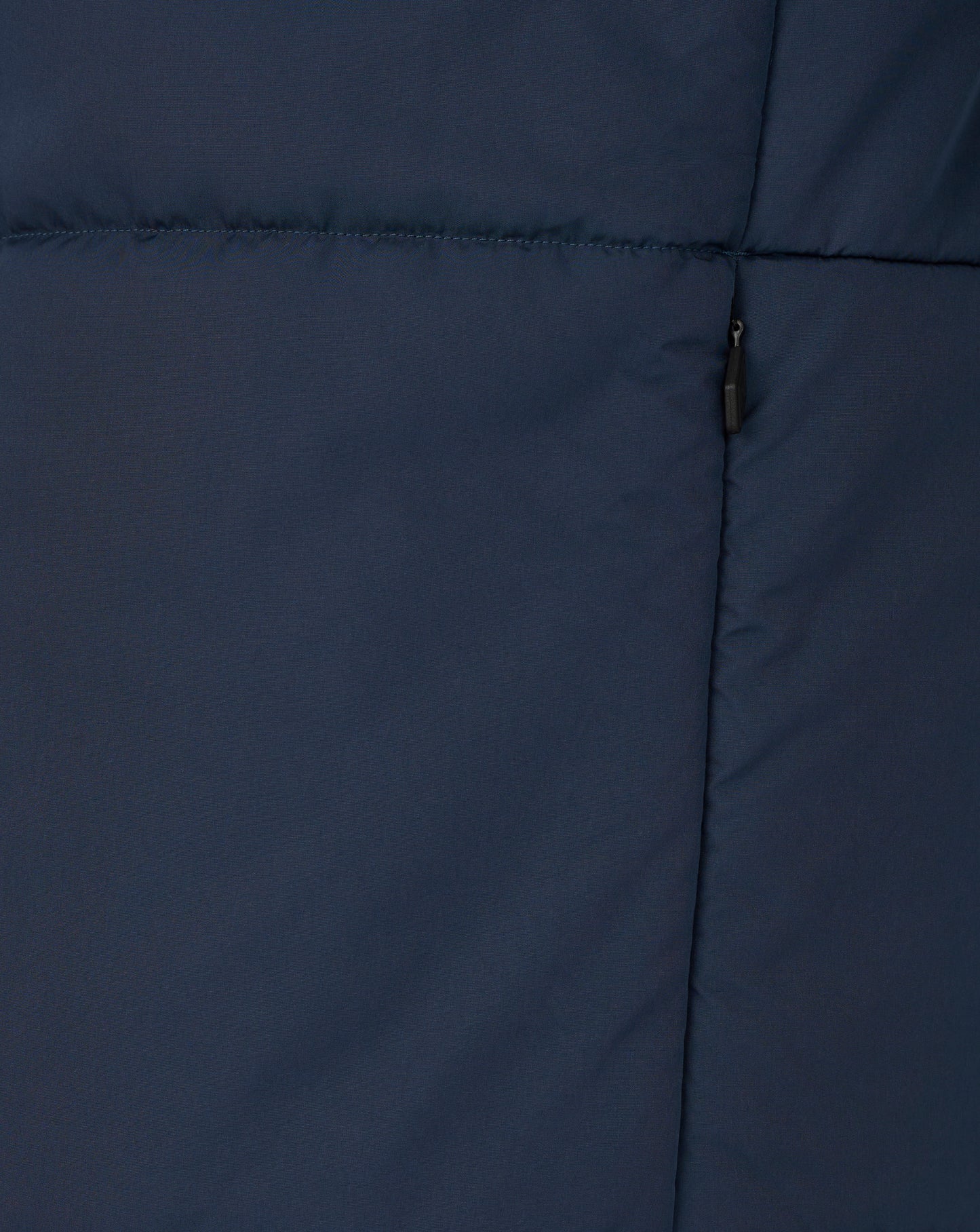 Close up of navy padded training jacket fabric with horizontal stitching and a black zipper pull