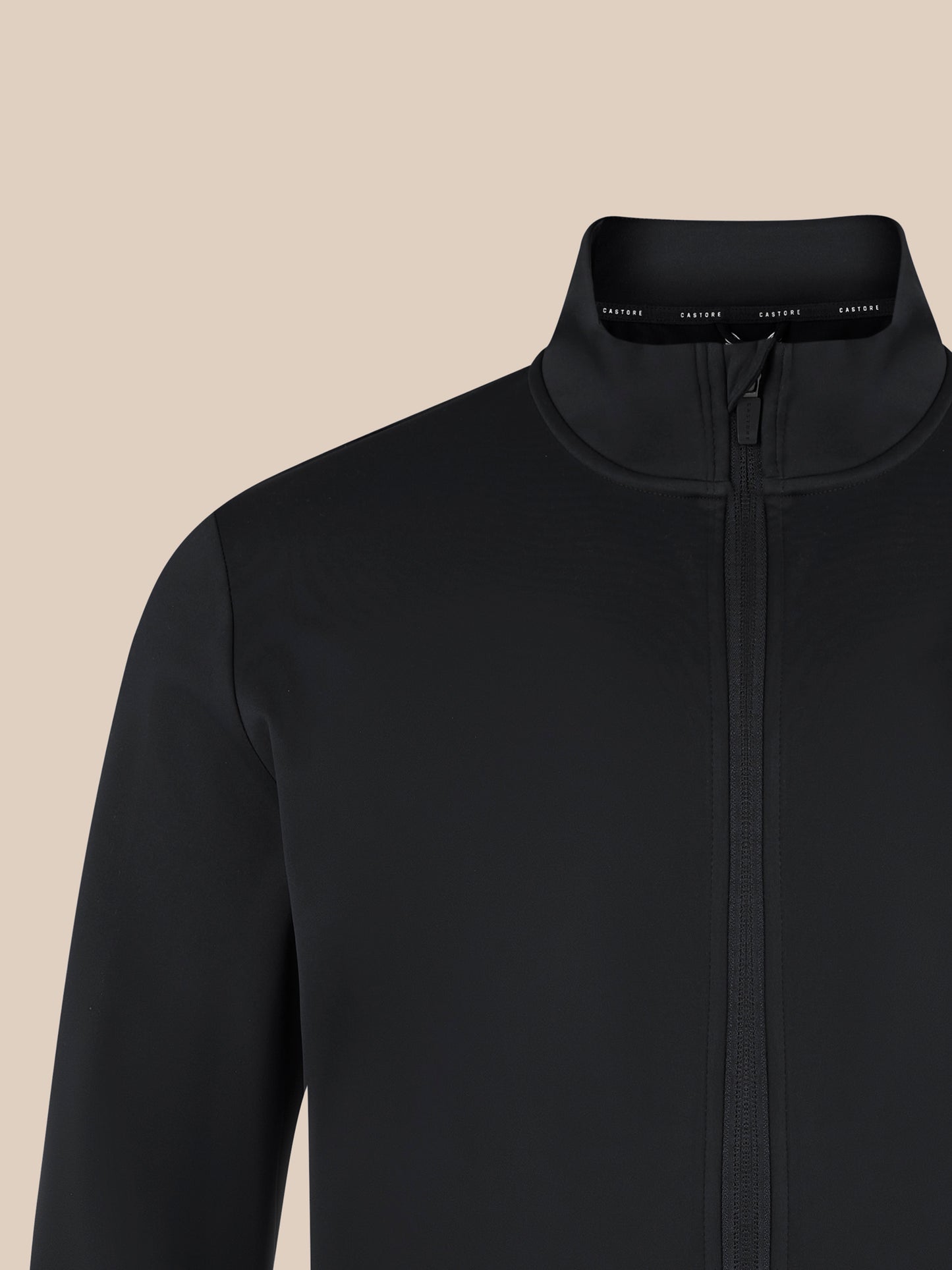 Close up of black unisex softshell jacket with high neck collar and front zipper on a beige background