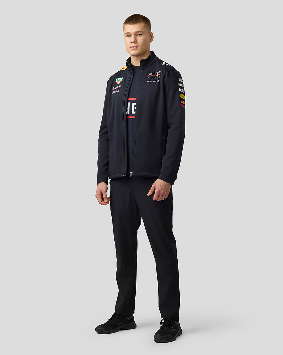 Full body shot of man in navy Night Sky Teamline Soft Shell Jacket with center zip and sponsor logos visible