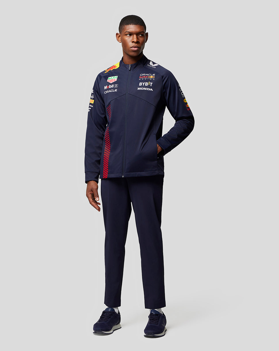 Full body shot of a male model wearing a navy Oracle Red Bull Racing soft shell jacket with multiple sponsor logos