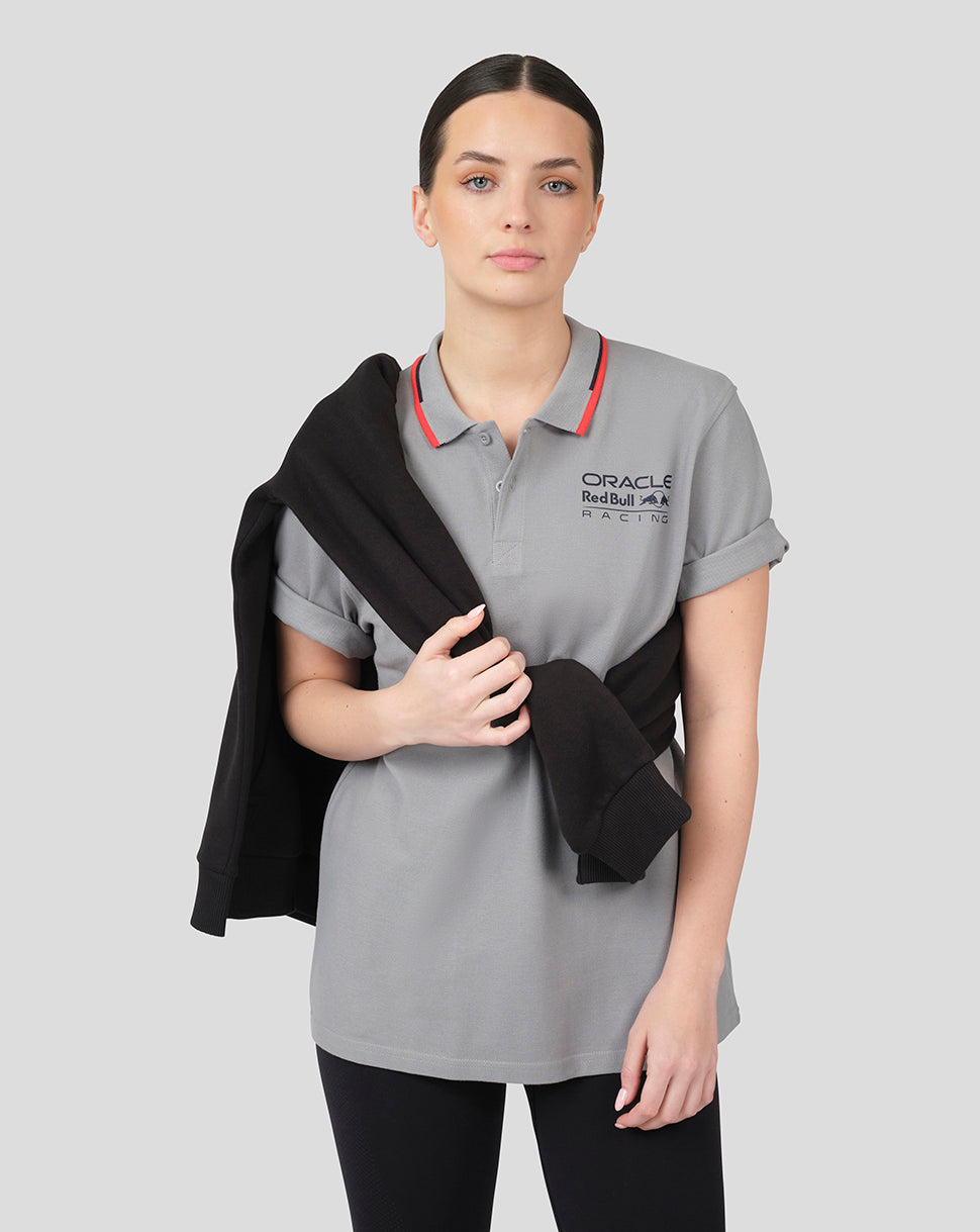 Female model wearing grey Oracle Red Bull Racing Core Polo with logo on the chest and a black jacket draped over her shoulder.