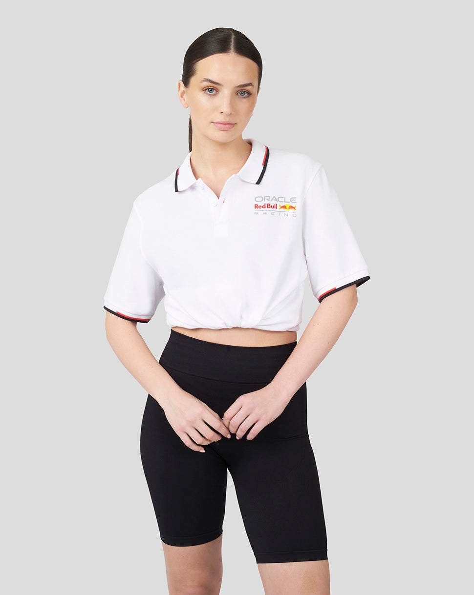 Female model wearing cropped white Oracle Red Bull Racing Core Polo with left chest logo and black shorts.