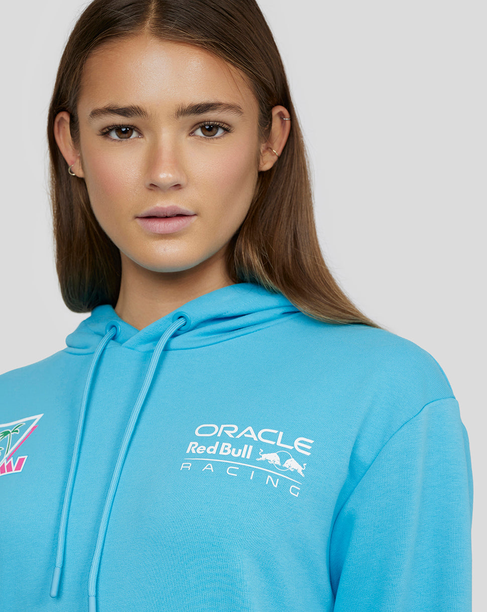 Portrait of a woman in a bright blue Oracle Red Bull Racing hoodie showing the front logo and drawstring hood