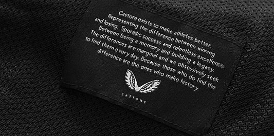 Close up of a Castore label sewn into black fabric showing the white Castore wing logo.