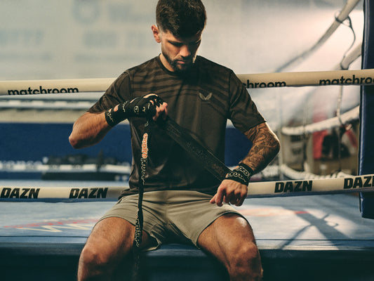 Male boxer in a dark athletic shirt with gloves stands inside a boxing gym