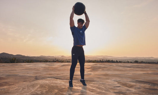 Athlete lifts a medicine ball overhead on a sunlit outdoor platform to illustrate strength training for sports performance