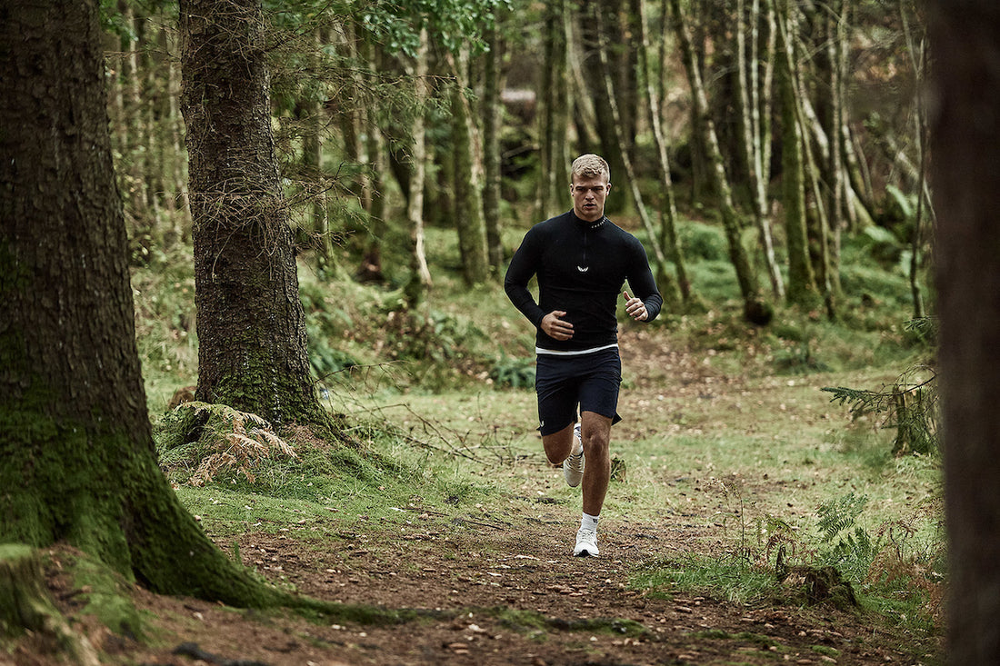 Runner on a forest trail wearing a black long sleeve top and dark shorts.