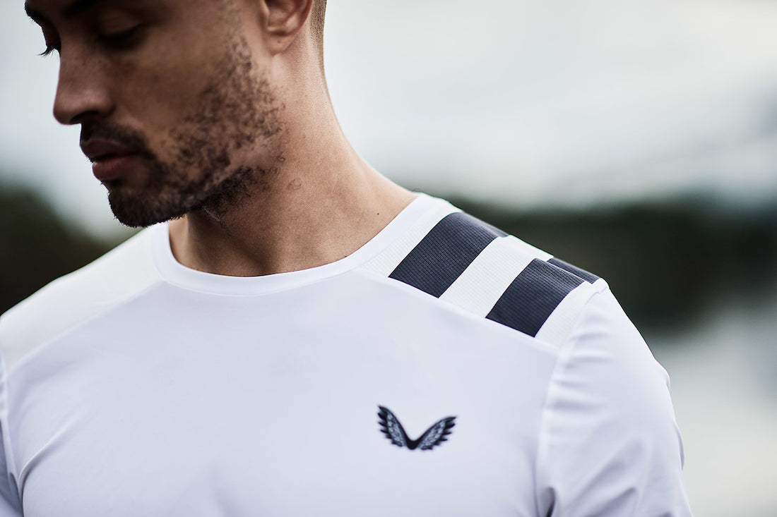 Close-up of a man wearing a white athletic shirt with dark shoulder stripes and a small wing logo on the chest.