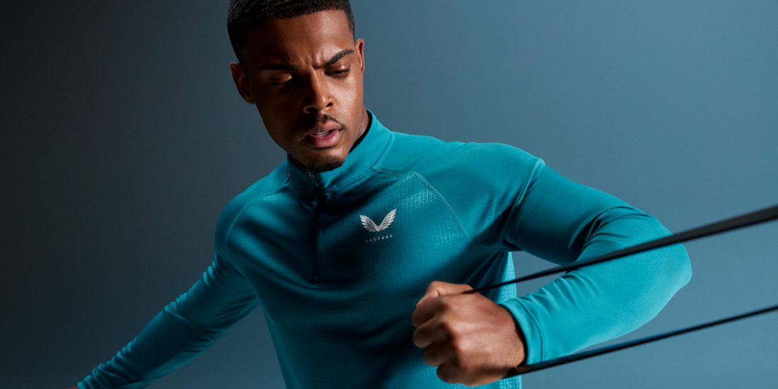 Male athlete in a teal sweat-wicking top uses resistance bands during a workout