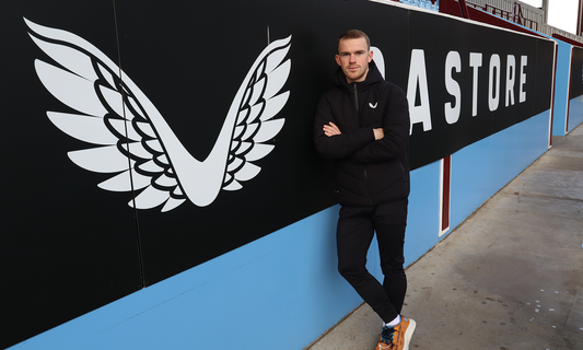Man in a black puffer jacket stands against a wall with a large white wing emblem and bold lettering