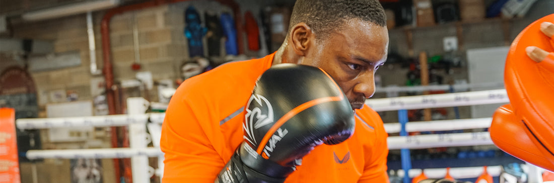 Boxer Dan Azeez trains in an orange top with black gloves inside a gym during a session.