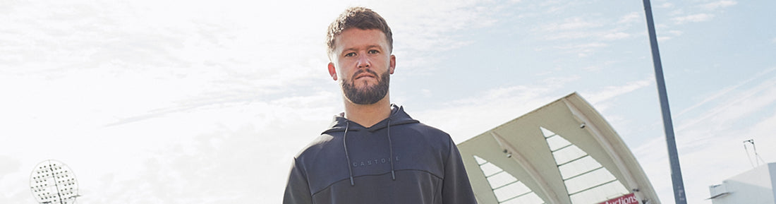Male athlete wearing a dark Castore hoodie outdoors at a sports complex.