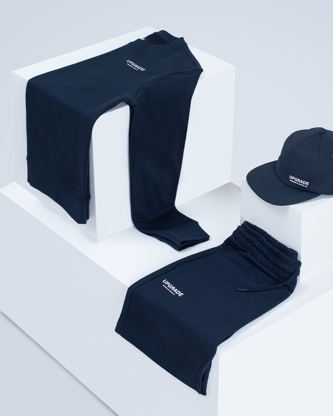 Navy track pants draped over white display blocks with a matching navy cap nearby